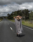 Person in a Estilo Emporio dress and hat walking alone on a long, straight road under a cloudy sky.
