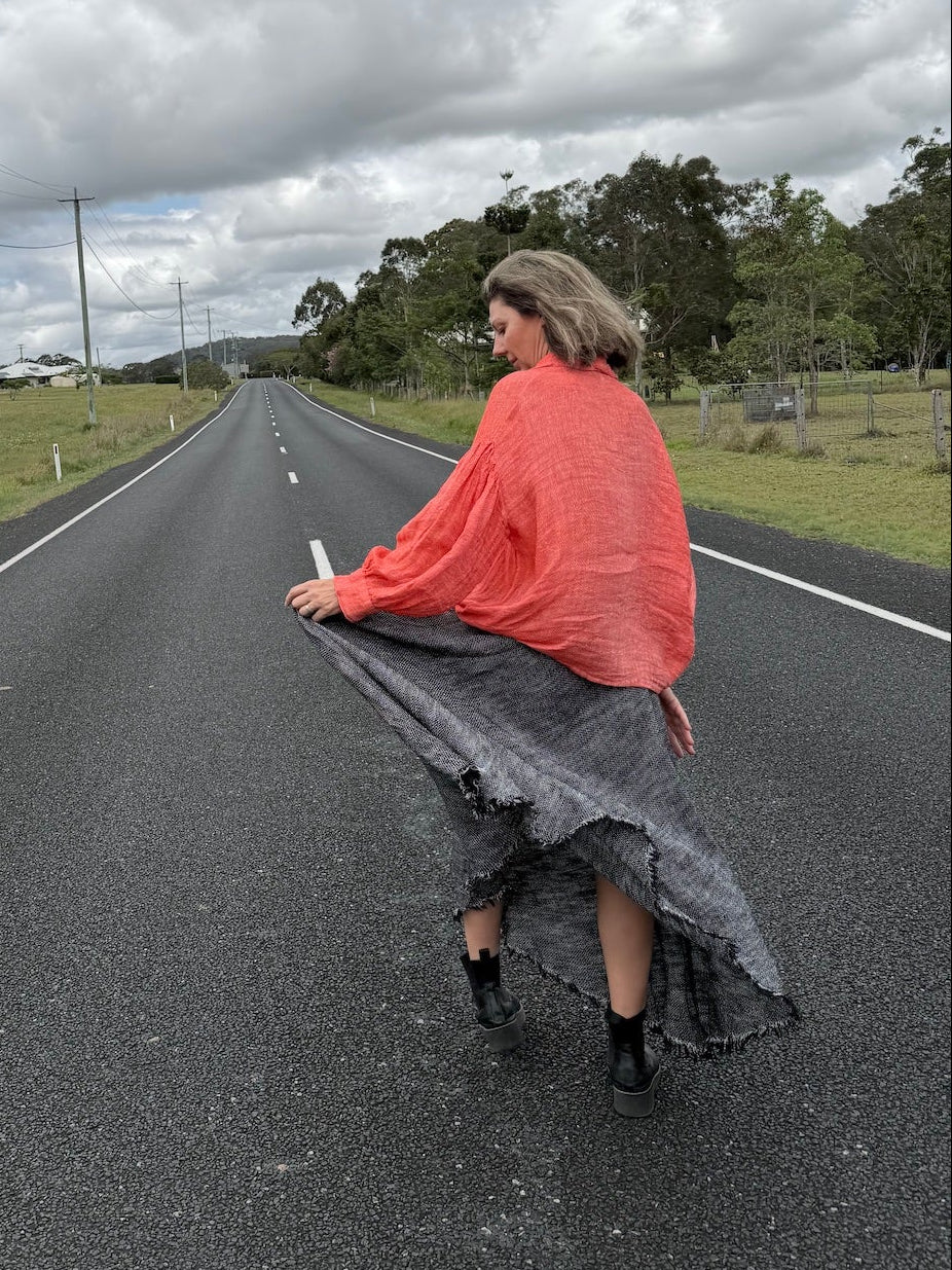 Person sitting on a road wearing estilo emporio dress, under a cloudy sky.