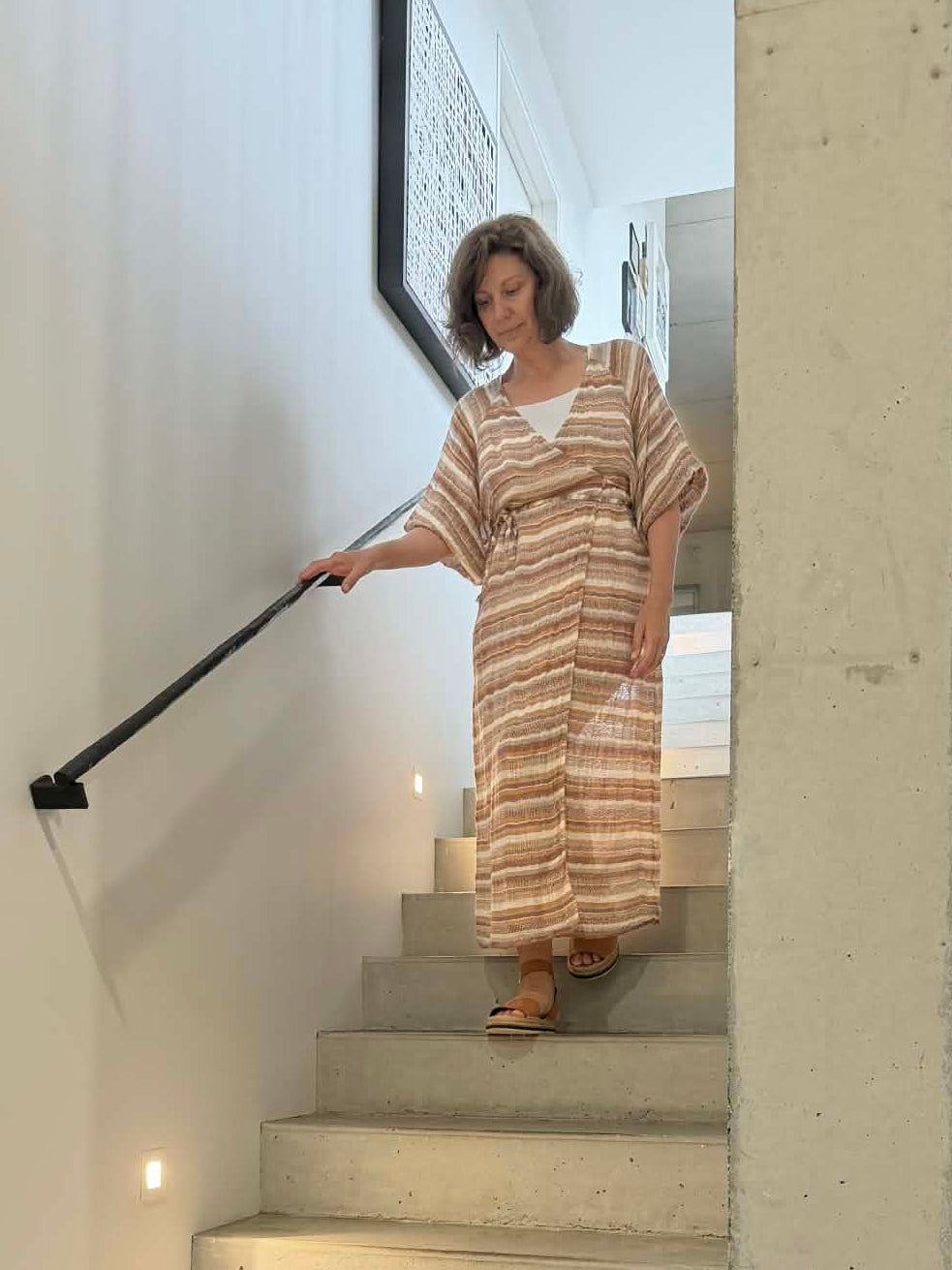 Woman descending a modern staircase wearing estilo emporio in a well-lit home interior.