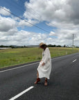 Person in a white linen dress standing on a road with a scenic background