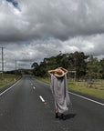 Person in a Estilo Emporio dress and hat walking alone on a long, straight road under a cloudy sky.