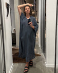 Woman taking a mirror selfie wearing a blue la bottega di brunella linen dress made in italy in a room with white walls and a gray floor.