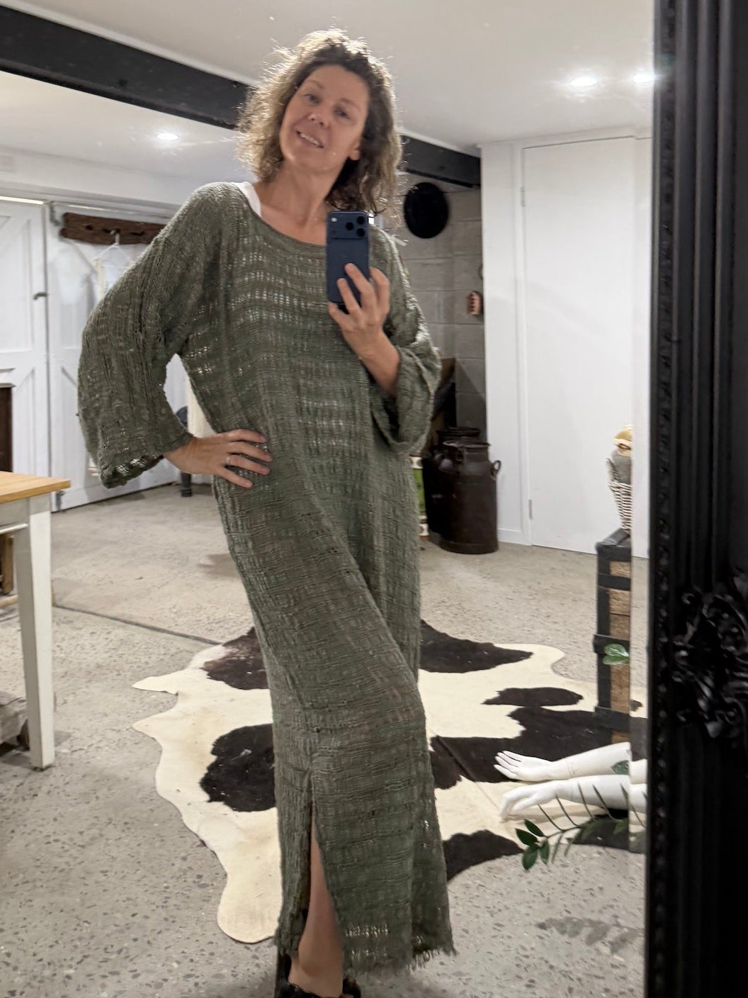 Woman taking a mirror selfie wearing a green  la bottega di brunella linen dress in a room with a cowhide rug.