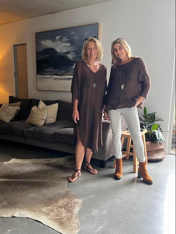 Two women standing in a modern living room with a gray sofa and decorative rug.