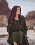 Woman in a green dress sitting on a log by a body of water