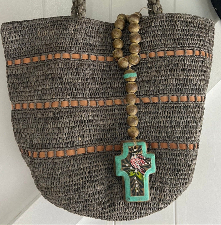 Made in Mada best-selling Alice bag, handcrafted from natural raffia, displayed against a wooden door alongside a stylish hat and decorative accents. A timeless, artisanal piece blending elegance with sustainable craftsmanship.